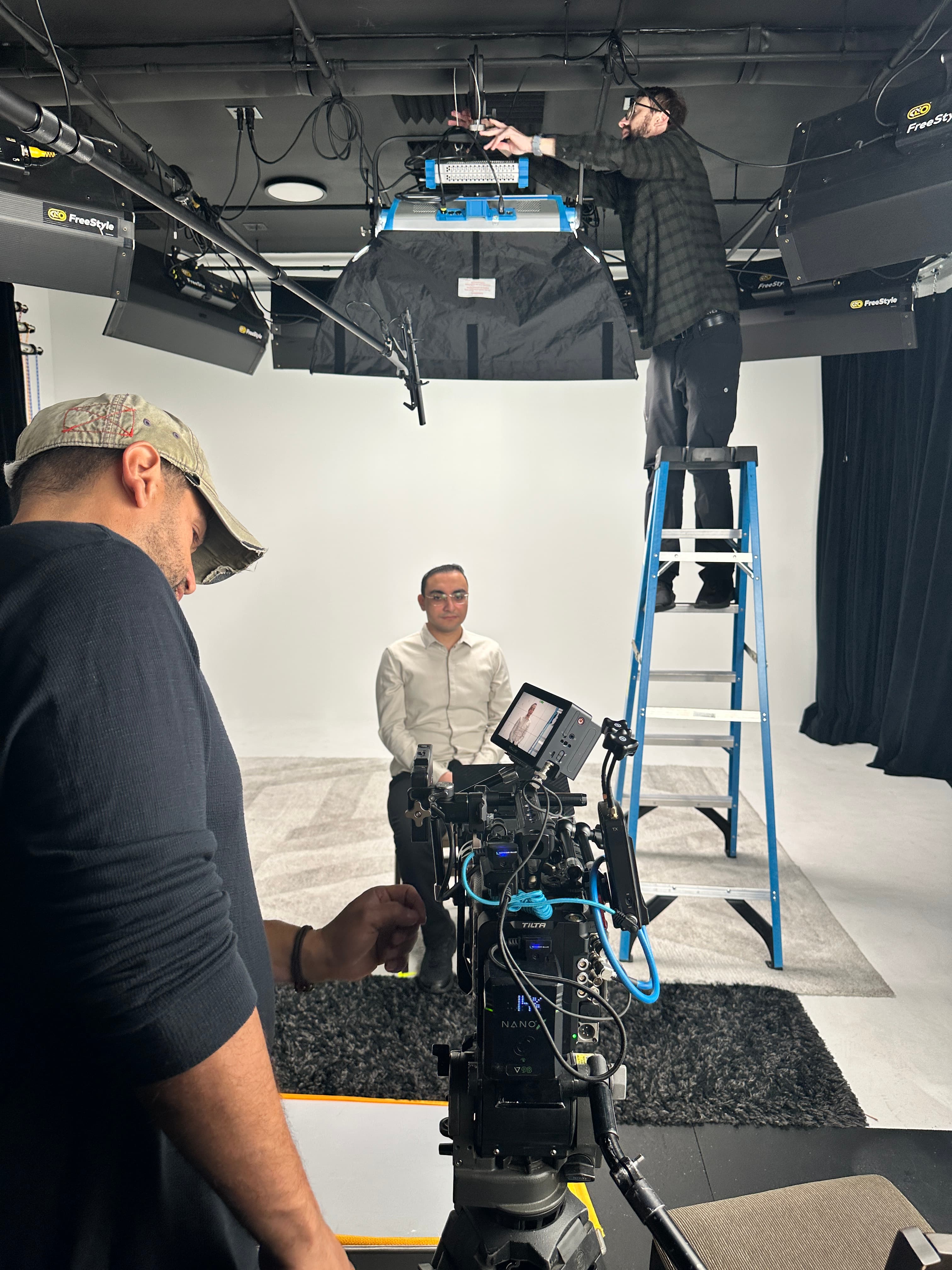 Crew preparing an interview setup beneath the studio lighting grid